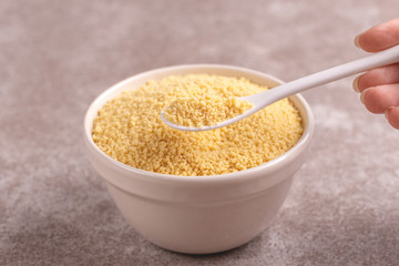 Full spoon of raw couscous grain in clay bowl