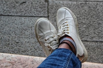 Closeup of a resting young girl's feet wearing white shoes and denims on an empty pavement