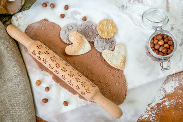 Rolling pin with a dog paw pattern on a wooden decorated table covered with baked flour. Rolled dough with a pattern and cookie of various shapes. Biscuit cooking background, top view