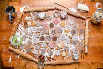 Different kind of rolling pin and cookie on a wooden decorated table covered with baked flour. Rolled dough with a pattern and cookie of various shapes. Biscuit cooking background, top view