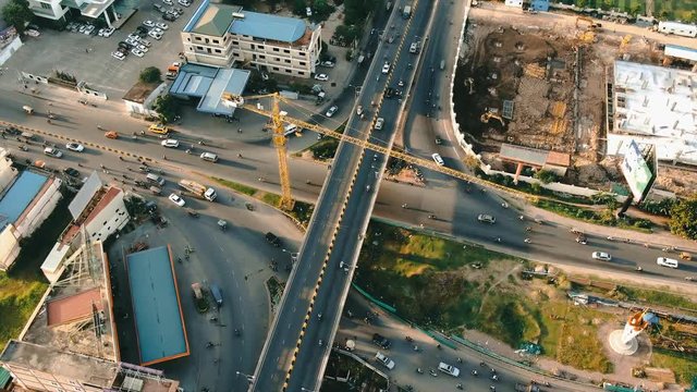 Aerial drone view circling above a busy overpass, onramp, roads, and flyway in Southeast Asia. Construction crane and construction can be seen nearby.