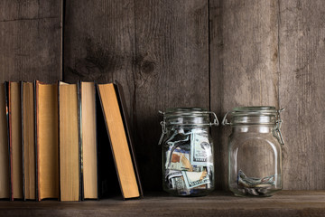 Two piggy banks, with different amounts of money and space for text, stand on a wooden bookshelf.