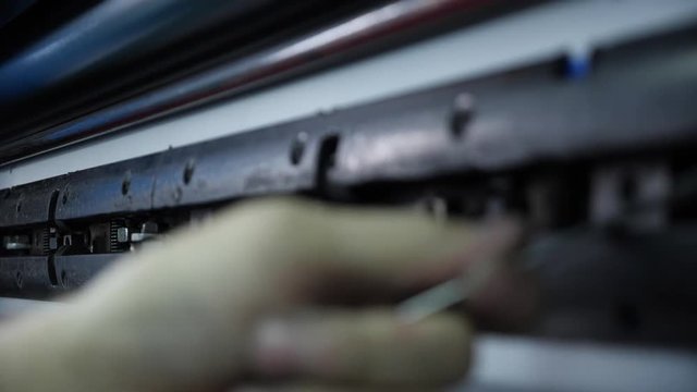 A printing worker inserts a form into the printing press with a tool. Mens hands with a special device serve the printing press.