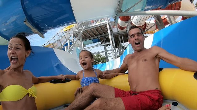 Family screaming and having fun while going down on a waterslide in a tube, filmed in slow motion