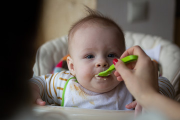 The first feeding of the baby from the spoon. Mom feeds baby homogenized chopped food with a spoon. child care.