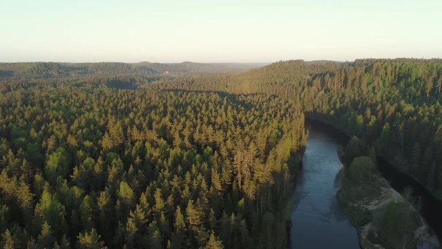 Aerial drone shot flying low over winding river and forests revealing valley during sunrise in Gauja National Park, Latvia
