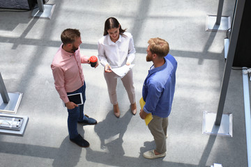 Top view of young modern people in smart casual wear discussing business while standing in creative office.