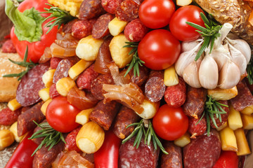 Set consisting of different varieties of sausage, meat, smoked cheese, tomatoes, pepper and bread as background