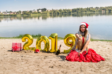 Woman in red dress sitting near golden balloons on the beach