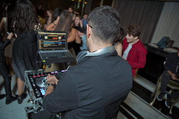 DJ with headphones at night club party under the colorful light and people crowd in background. Dj...