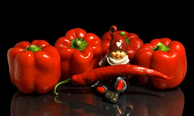 close up of four red bell paprikas and a gnome holding a red chili pepper with reflection on black background, still life.