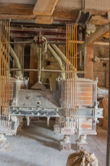 Portrait format of traditional flour mill equipment, covered in flour from milling, with shutes feeding mill with organic grain and a full bag of flour on floor in front.