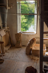 Traditional artisan wooden flour mill feeding flour bags with freshly ground flour and bags of flour on floor, with light shining through window in background