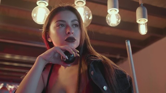 Portrait of sexy brunette woman in lingerie and jacket posing with pool cue ball and stick on the bar table in luxurious modern interior - video in slow motion