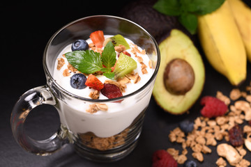 Close up yogurt with granola and fruits in glass on black granite stone table