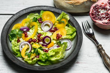 Healthy lunch, fresh salad with the addition of purple onion and pomegranate seeds on white, wooden background
