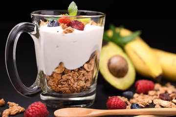 Yogurt with granola and fruits in glass on black granite stone table