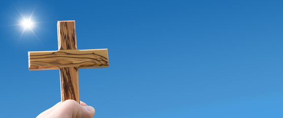 preacher holding wooden cross against blue sky