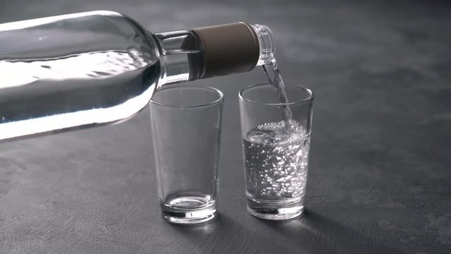 Vodka pouring from a bottle into a glass in a black background. Pouring vodka in glasses close-up. Vodka being poured into a glass