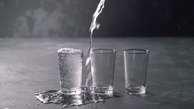 Vodka pouring from a bottle into a glass in a black background. Pouring vodka in glasses close-up. Vodka being poured into a glass