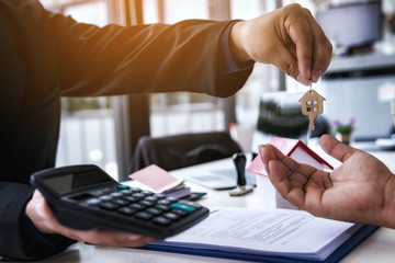 Real estate agent handing over a house key on the rental agreement or the buy home contracts with the real estate property. Mortgage concept.