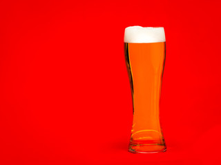 Tall glass of pale ale or beer with head on red background