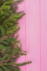 Christmas fir branches border on the left side. Christmas evergreen border on pink wooden boards with copy space. Winter holiday card.
