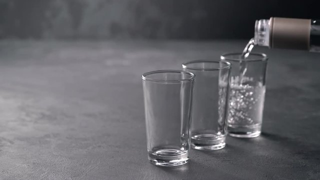 Vodka pouring from a bottle into a glass in a black background. Pouring vodka in glasses close-up. Vodka being poured into a glass