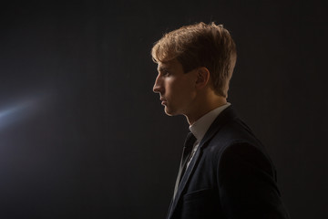 Profile of a young man in a business suit on a black background.
