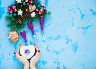 Beautiful Christmas decorations, tree and gift in woman's hands on the blue background. Flat lay, top view, close up space for a text.