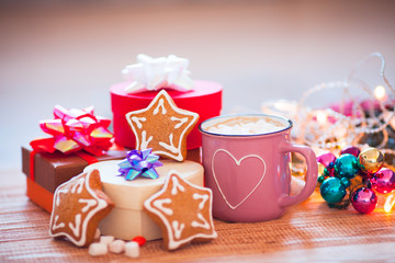 Cup of chocolate with marshmallow, gingerbread cookies, gifts and beautiful Christmas decorations with lights on the wooden background. Flat lay, top view, close up space for a text.