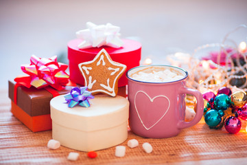 Cup of chocolate with marshmallow, gingerbread cookies, gifts and beautiful Christmas decorations with lights on the wooden background. Flat lay, top view, close up space for a text.