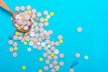 Top view of pharmaceutical medicine pills, capsules and tablets w/ wooden spoon on light blue background. Vitamin and supplement. Health behavior concept. Minimal style. Creative idea.