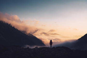 Silhouette of a woman standing on a ridge, enjoying the sunset.