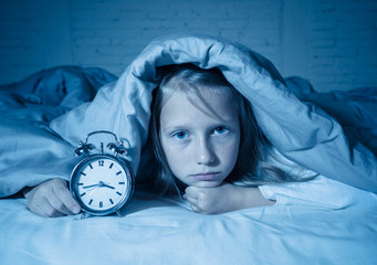 Little girl suffering from insomnia looking at alarm clock feeling desperate sad and restless