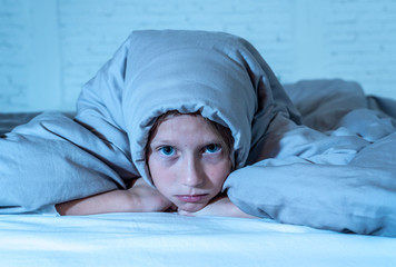 Beautiful little girl feeling sad and tired not being able to sleep at night covering head under duvet