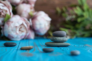 Pyramids of gray zen pebble meditation stones with green leaves and beautiful fresh peony flowers on wooden background. Concept of harmony, balance and meditation, spa, massage, relax