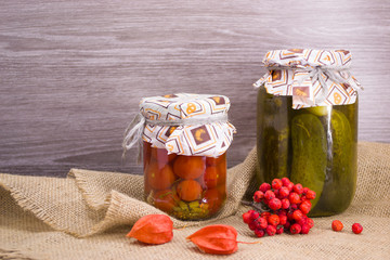 Salted tomatoes, Pickles  in glass jars and Rowan and physalis berries on a wooden background.