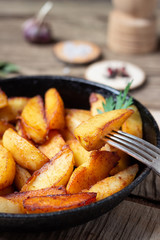Fried potatoes wedges in a pan on wooden table.