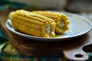 un épi de maïs jaune servi avec du beurre sur une assiette blanche, un repas sain