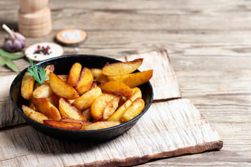 Fried potatoes wedges in a pan on wooden table.