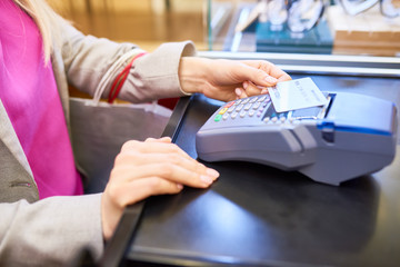 Closeup of unrecognizable young woman paying via credit card using NFC technology in shopping mall or cafe, copy space