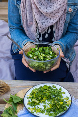Young woman hands holds on legs fresh green salad with spinach, cucumbers in glass bowl. Vegan food, vegetarian lunch, healthy paleo diet