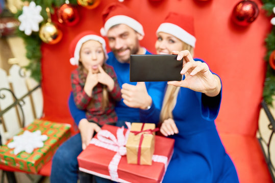 Woman using phone to take selfie with happy family enjoying Christmas celebration in shopping mall