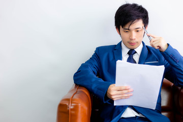 Charming handsome young guy is thinking his work for solving problems. Attractive handsome businessman hold paperwork and pen. He is professional and expert of business. He looks clever. copy space