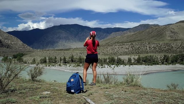 Young happy torist woman is standing to the edge of the mountain and taking photo scenic landscape. Back view, slider