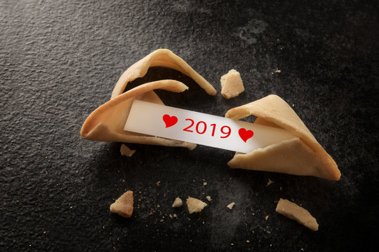 broken chinese fortune cookie with 2019 and red hearts on the paper slip on a dark background with copy space, new year concept, high angle view from above