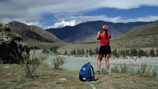 Young torist woman is standing to the edge of the mountain and taking photo scenic landscape. Back view, slider