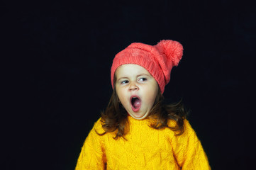 Portrait of a little emotional girl on a dark background . Girl in hat and sweater