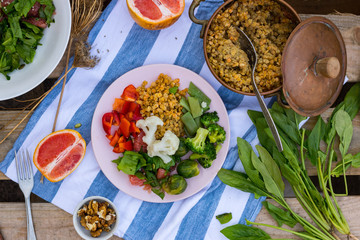Woman hand holds buddha bowl plate with red pepper bell salad, cooked vegetables (broccoli, brussels sprouts, cauliflower), spinach, grapefruit, Indian traditional lentil. Vegan vegetarian food